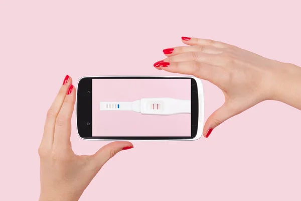 Female hand with red fingernails holding smartphone with positive pregnancy test — Φωτογραφία Αρχείου