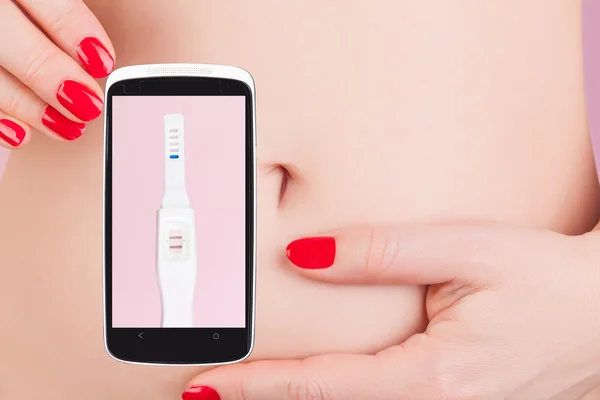 Woman with red nails holding mobile phone with pregnancy test — 图库照片