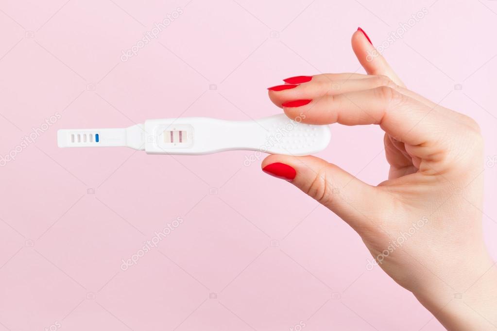 female hand with red fingernails holding positive pregnancy test