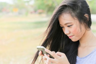 bir cep telefonu kullanarak bahçede oturan genç Asyalı kadın