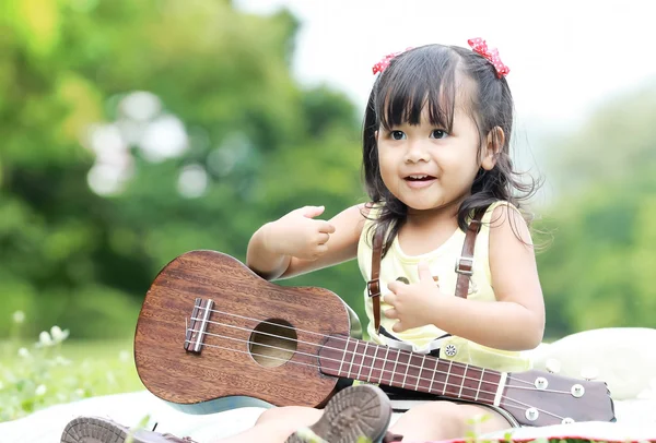 Дівчина сидить на траві і грає укулеле в саду — стокове фото