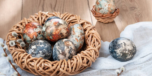 Easter composition - Easter eggs painted with natural dyes in a wicker nest on a wooden table