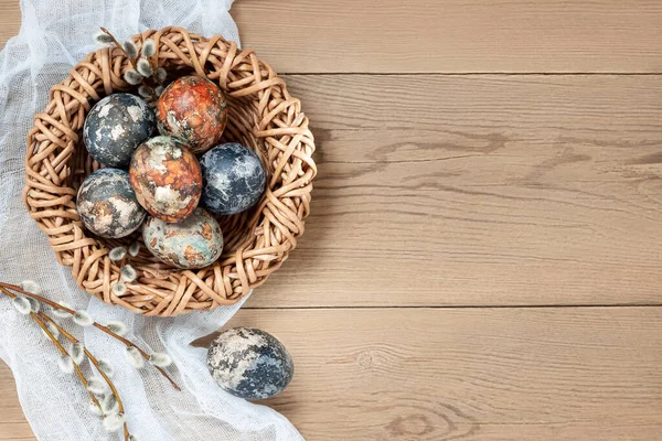 Osterkomposition - mit natürlichen Farbstoffen bemalte Ostereier in einem Weidennest auf einem Holztisch, Kopierraum — Stockfoto