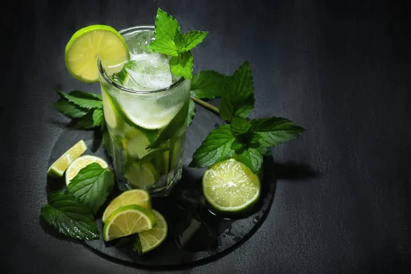 Fresh homemade mojito cocktail in a tall glass with lime, mint and ice on a black table, copy space — Zdjęcie stockowe
