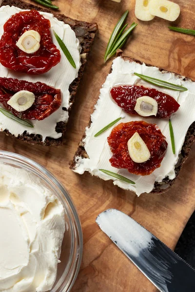 Sandwiches caseros de pan multigrano con queso crema y tomates secados al sol en una bandeja de madera. Concepto de alimentación saludable. Imagen vertical — Foto de Stock