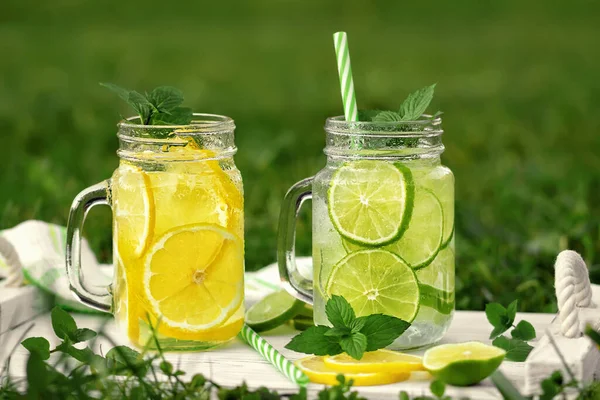 Zimna, orzeźwiająca lemoniada domowej roboty z miętą, cytryną i limonką w słoikach murarskich na letnim trawniku — Zdjęcie stockowe