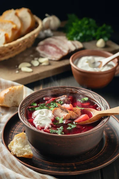 Borscht recién cocido - plato tradicional de la cocina rusa y ucraniana en plato de barro con tocino, crema agria y ajo, imagen vertical Imagen De Stock