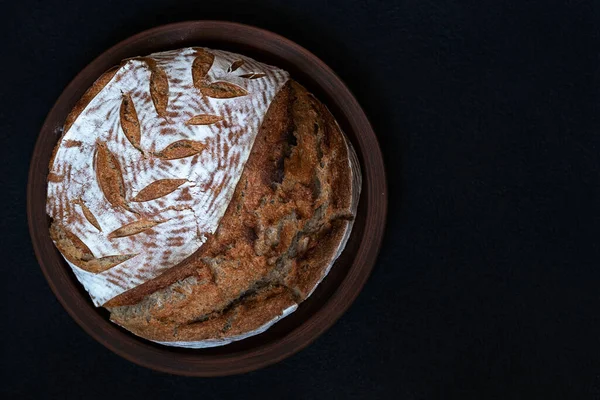 Pão escuro redondo caseiro com crosta de farinha e espigueta pintada em uma placa de barro. Vista superior com espaço de cópia — Fotografia de Stock