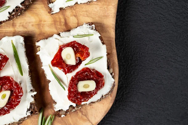 Sandwiches caseros de pan multigrano con queso crema y tomates secados al sol en una bandeja de madera. Concepto de alimentación saludable. Copyspace, plano, vista superior — Foto de Stock