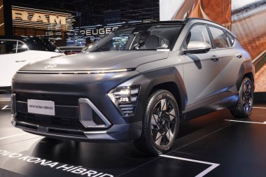 Hyundai Kona hibritinin ön görüntüsü, sağlam bir tasarım, LED ışıklandırma, modern tekerlekler ve bir otomobil fuarında mat bitirme.