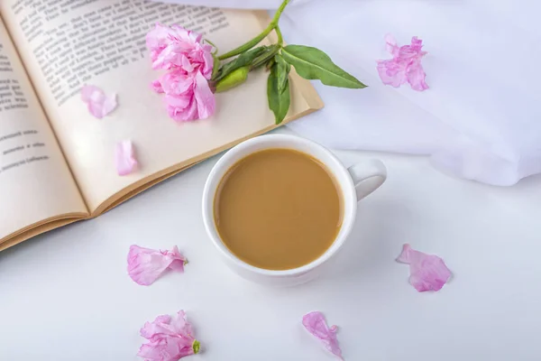 Romantic vintage still life with pink flowers, old book, cup of tea or coffee in spring, summer day in garden. Coffee time