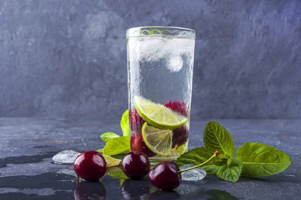 Glass of Summer lemonade or ice tea. Refreshing cool detox drink with cherry and mint on dark background.Mojito cocktail with ice cubes. Healthy eating. opy space for text