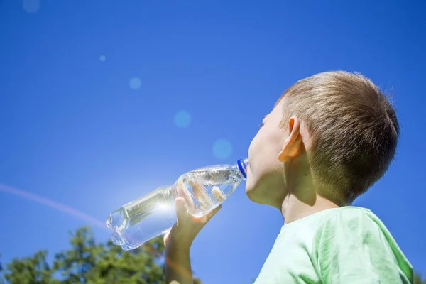 青空に対してプラスチックボトルから純粋な澄んだ水を飲む小さな男の子6 スポーツ活動の後の暑い夏の日に喉の渇きの子供 — ストック写真