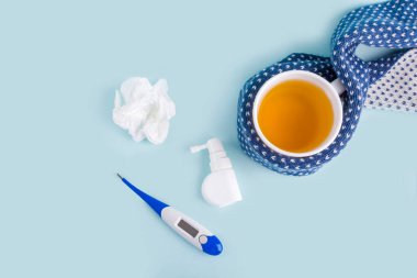 Bir fincan papatya çayı, termometre, buruşmuş peçete ve mavi arka planda akan burun ve boğaz için sprey. Mevsimsel hastalıklar ve soğuk algınlığı, grip, sıcaklık tedavisi. Virüsün önlenmesi, metin için boşluk kopyala