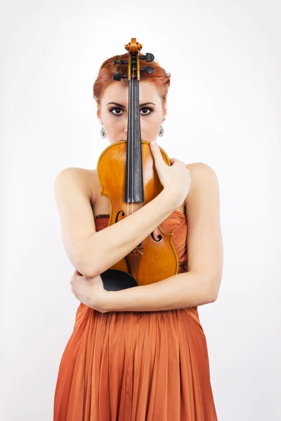 Joven chica pelirroja con un violín en las manos sobre un fondo blanco. vestido de noche. Vestido largo de color naranja —  Fotos de Stock