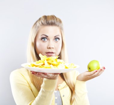 Blonde girl chooses between an apple and potato chips. Healthy food and harmful. Delicious food is unhealthy