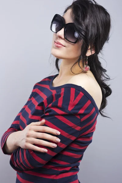 Beautiful brunette in a blue dress with red stripes. Fashion. Portrait of a young girl in sunglasses. — Stock Photo, Image