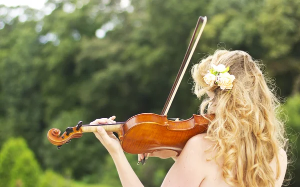 Красивая улыбающаяся девушка играет на скрипке на открытом воздухе. Музыкант для свадьбы. Скрипка под открытым небом — стоковое фото