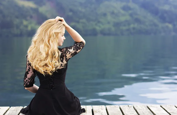 Mooie blonde vrouw met luxe haren op het meer. Portret van een jonge vrouw in een zwarte avondjurk met kant. Mooie witte krullend haar — Stockfoto