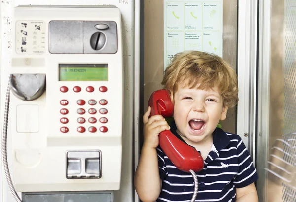 Маленький мальчик кричит в телефон. Мальчик кричит в красный телефон — стоковое фото