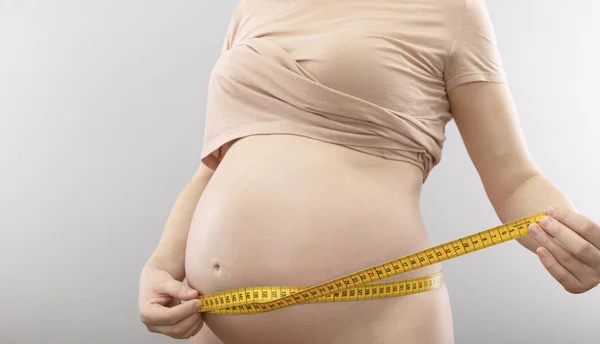 Беременная Женщина Измеряет Свой Живот Изолированным Сером Фоне — стоковое фото