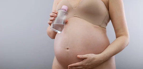 Těhotná Žena Drží Tělesný Olej Strie Těhotné Břicho Izolované Šedém — Stock fotografie