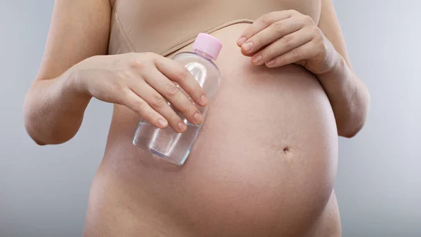 Těhotná Žena Drží Tělesný Olej Strie Těhotné Břicho Izolované Šedém — Stock fotografie