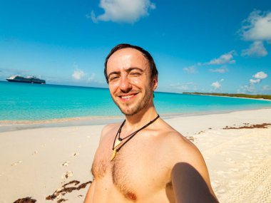 Gülümseyen adam sahilde selfie çekiyor.