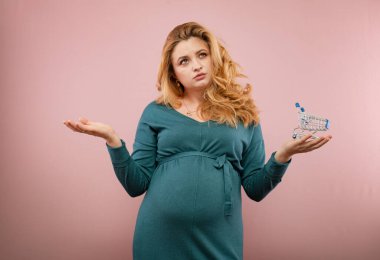 Yeşil elbiseli hamile kadın pembe bir arka plan düşünüyor. 