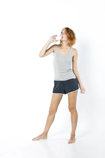 Mladá hubená holka pije vodu v dopoledních hodinách. portrét krásné zrzavý dívku na bílém pozadí — Stock fotografie