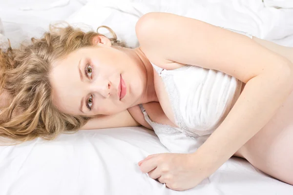 Mladá těhotná žena luxuriates v bílé posteli. — Stock fotografie