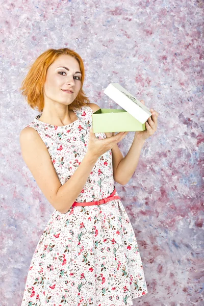 Jong meisje met rode haren met een gift op een lichte achtergrond. Portret van een mooi meisje. — Stockfoto