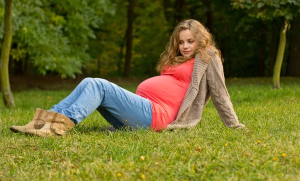 美丽怀孕的金发美女躺在绿色的草地上。怀孕的女人的肖像。户外活动 — 图库照片
