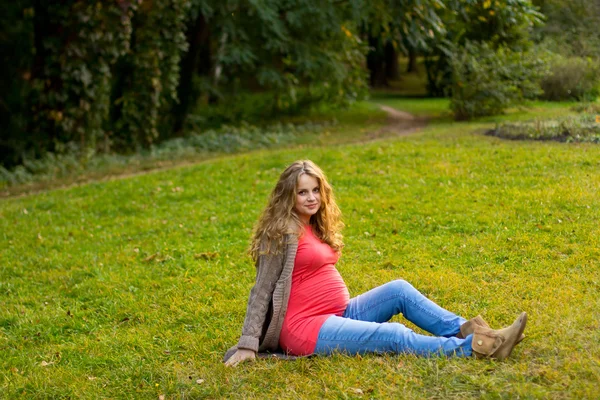 美しい妊娠中のブロンドは緑の芝生の上に横たわる。妊娠中の女性の肖像画。アウトドア — ストック写真