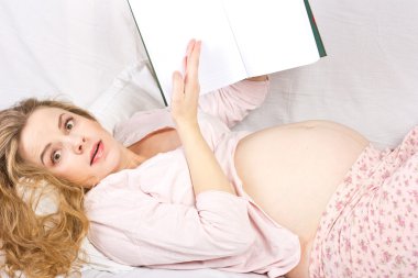 Güzel hamile sarışın yatakta kitap okuyorum. Hamile kadın portresi