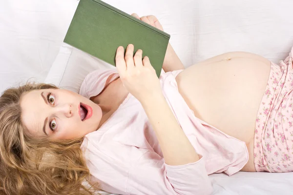 Piękna blondynka w ciąży, czytanie książki w łóżku. Portret kobiety w ciąży — Zdjęcie stockowe