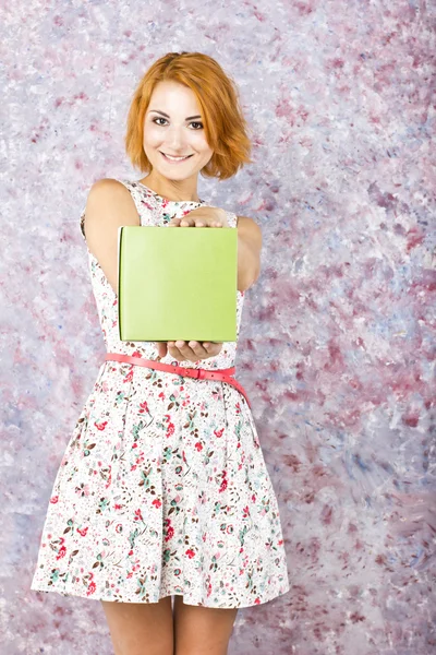 Schöne schlanke Mädchen in einem kurzen Kleid hält Geschenkbox. bunter Hintergrund. Porträt eines rothaarigen Mädchens — Stockfoto