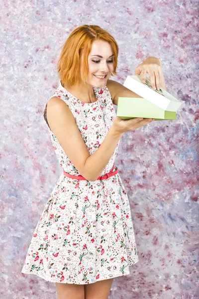 Krásná štíhlá dívka v krátkých šatech drží krabičky. Barevné pozadí. Portrét rusovlasá dívka — Stock fotografie