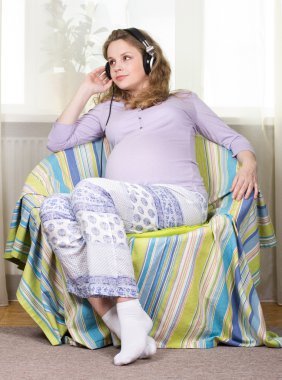 Beautiful pregnant blonde listens to classical music on headphones. Portrait of pregnant woman. The development of the child in the womb clipart