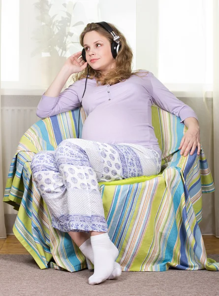 Красивая беременная блондинка слушает классическую музыку в наушниках. Портрет беременной женщины. Развитие ребенка в утробе матери — стоковое фото