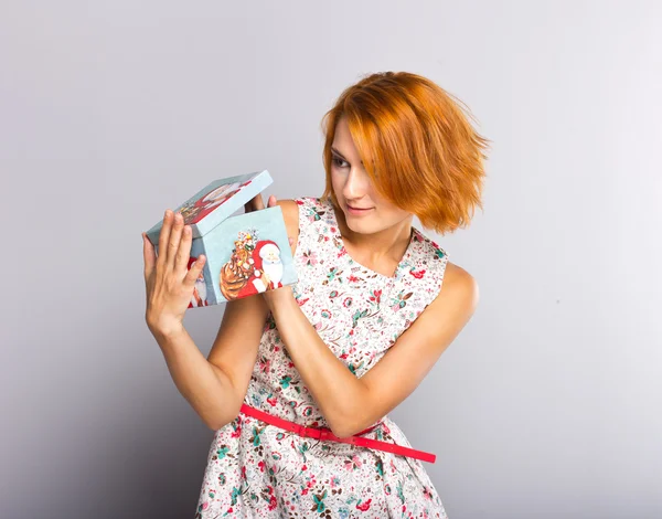 Schöne rothaarige Mädchen mit Geschenkbox in den Händen. Porträt der schönen jungen Mädchen in einem kurzen Kleid — Stockfoto