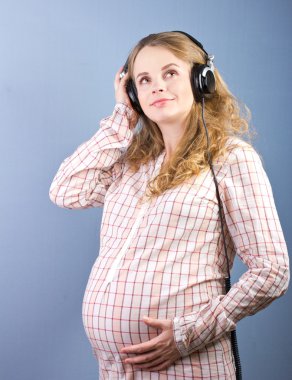 Young pregnant woman listening to music on headphones at home closed. Portrait of pregnant woman clipart
