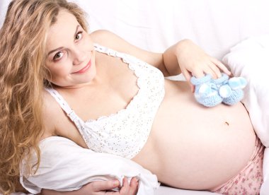 Beautiful pregnant blonde woman with booties in her hand clipart