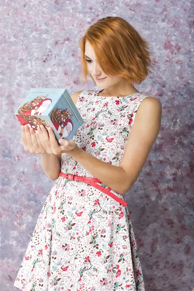 Mooi roodharig meisje met de doos van de gift in handen. Portret van mooie meisje in een korte jurk — Stockfoto