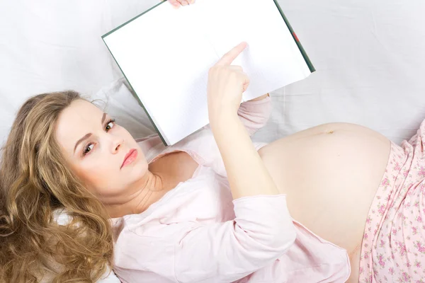 Vacker gravid blondin läser en bok i sängen. Porträtt av gravid kvinna — Stockfoto