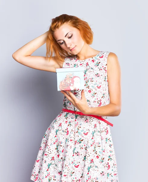 Vakker, slank jente i kort kjole med gaveeske. Fargerik bakgrunn. Portrett av rødhåret jente – stockfoto