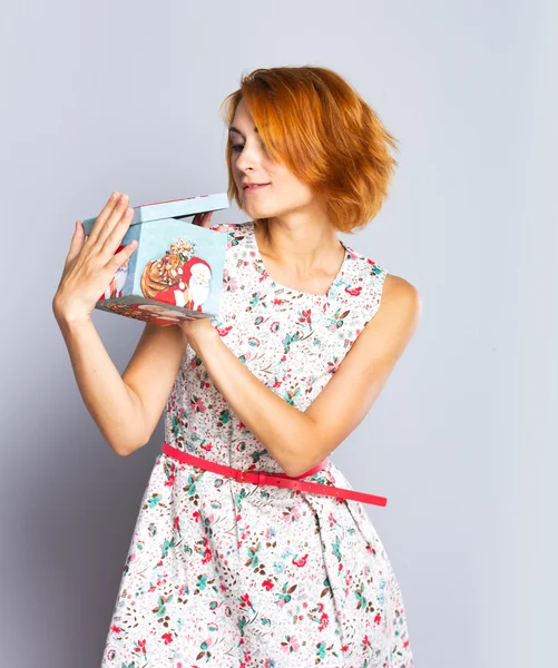 Vacker smal tjej i en kort klänning holding presentförpackning. Färgstark bakgrund. Porträtt av rödhåriga flicka — Stockfoto