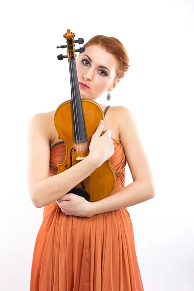 Joven chica pelirroja con un violín en las manos sobre un fondo blanco. vestido de noche. Vestido largo de color naranja —  Fotos de Stock