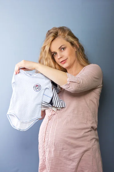 Mooie blonde zwangere vrouw met kleren van de baby. De kleren van kinderen. Zwangere blonde. Portret van de zwangere vrouw — Stockfoto