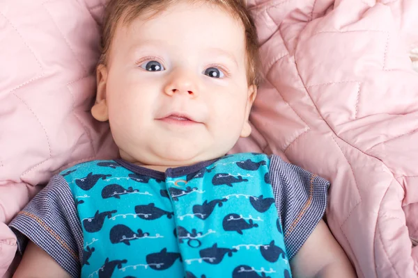 Cute baby w łóżku, różowy. Portret dziecka. Portret uśmiechniętego dziecka. Dziecko na białym łóżku. Przystojny chłopak. — Zdjęcie stockowe